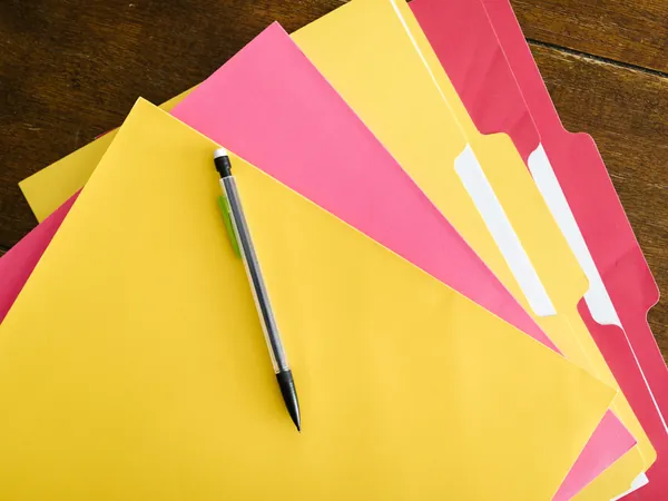 Coloured file folders and a pencil on a wooden table
