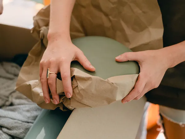 Hands wrapping a fragile item in brown packing paper