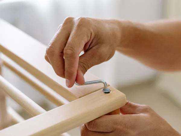 Hands loosening a bolt in a wooden furniture frame with an Allen key